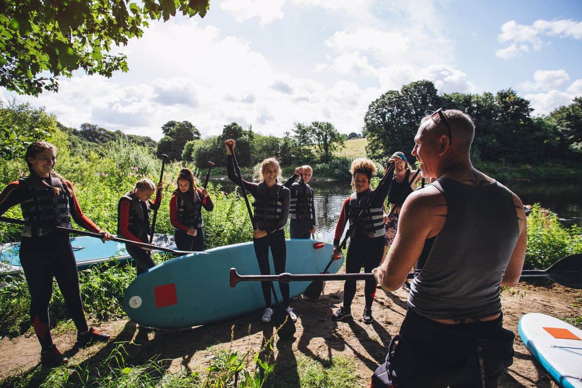 Fachkraft begleitet in der Erlebnispädagogik Jugendliche beim Stand-Up Paddeln im Rahmen der Ergänzenden Angebote bei der Karl Immanuel Kuepper-Stiftung